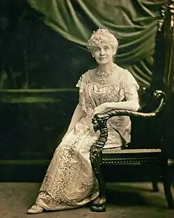 A seated woman with short hair wearing a white dress