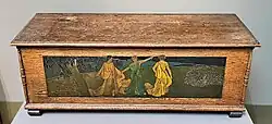 Large wooden chest decorated with a painted carving of three women standing in a landscape.