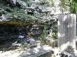 A memorial slab in a lush environment near a rockycliff overhang
