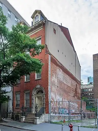 The facade of the Merchant's House Museum as seen from Fourth Street. To the left is the main facade, which faces south, and to the right is the eastern facade. The main facade has three bays of windows, with a stoop ascending to the main entrance in the rightmost bay. The eastern facade is made of plain brick and stucco and is covered in graffiti.