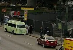 Multiple people wait on the sidewalk of Puerto Aéreo Boulevard, next to the station entrance.
