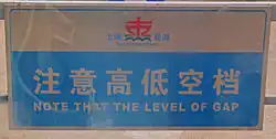 A light-colored sign with Chinese characters and "Note that the level of gap" written on it in blue