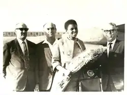 Makeba standing before an aeroplane flanked by three men