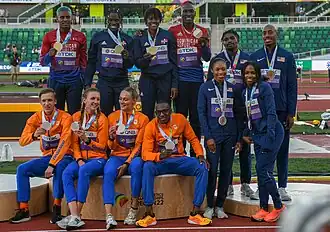 Photo of twelve standing or sitting athletes from three nations wearing tracksuits and holding their medals