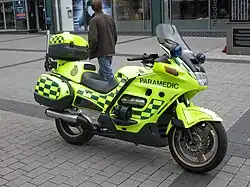Yellow motorcycle with green battenberg livery parked without rider on a pavement.