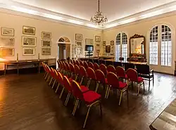 A spacious room with rows of red chairs and a speakers' table at the front
