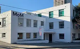 Photograph of Museum of Museums, a white rectangular three-story building with "MoM" painted on it.