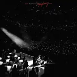 A black-and-white picture of Raye playing piano alongside an orchestra and in front of a crowd at the Royal Albert Hall