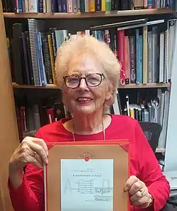 Woman with bookshelf behind her holding up a paper