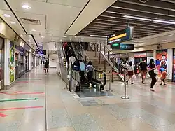 View of the NEL platforms with an escalator going upwards. Two prints are on the opposite sides of the platform, on the pillars in between the platform screen doors.