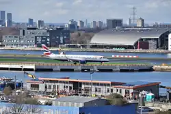 A view looking across the King George V Dock in East London showing the building of the new RNLI Tower Lifeboat Station with a British Airways plane at London City Airport in the background. Image dated 17th March 2023