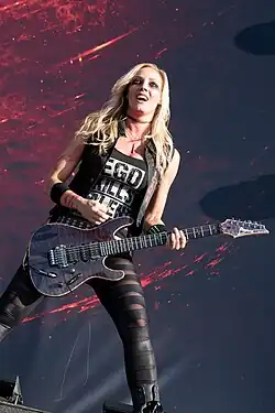 Nita Strauss playing an electric guitar in a black outfit with dark make up.
