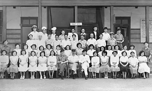 Four rows of people, mostly in civilian clothes, some in military dress, in front of a building marked "Transit Hotel"