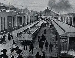 Several workers stand among trains and buildings with shovels in their hands