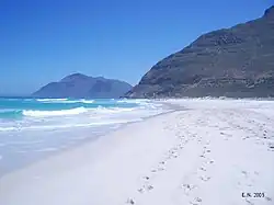Looking north along the beach. The slopes of Chapman's Peak rise to the right at the end of the sand. The peak in the distance is Karbonkelberg, west of Hout Bay