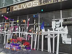 Twenty-six crosses bearing the names of the deceased are displayed on the protective fence of Olivos station.