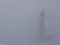 Statue of Madonna surrounded by fog in mountainous setting