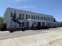 A gray art deco-style building with a black sparrow imprint on it. Yucca plants in planters stand in front of the building.