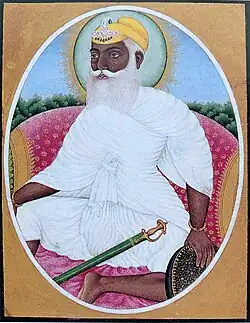 A color portrait of a bearded and turbaned man wearing white clothes and seated on a throne