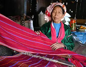 A Palaung woman weaving a vibrant fabric on a lap loom.