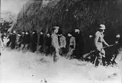 Soldiers putting blindfolded people up against a wall
