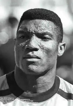 black male with distinguished square features and uniquely pock-marked face, short afro hair and wearing sporting jersey