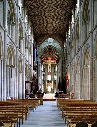 The nave of Peterborough Cathedral (1118–1193) in three stages of arcade, gallery & clerestory, typical of Norman abbey churches. The rare wooden ceiling retains its original decoration (c. 1230). Gothic arches beneath tower (c. 1350).