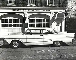 1960s white sedan parked in front of a brick building