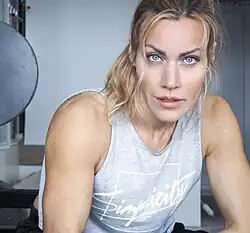 close-up of Silje Torp wearing a gray print tank top, appearing to sit on a gym bench, staring intently at camera