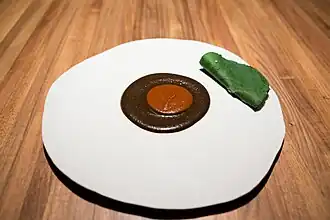 A plate with two types of mole served one on top of the other. They are accompanied by a Mexican pepper leaf.