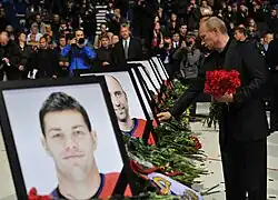 Vladimir Putin placing red flowers along a row of large framed photos of the deceased Lokomotiv hockey players.