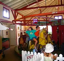 A girl in a green shirt reaching for a brass ring dispenser while riding on a red historic carousel