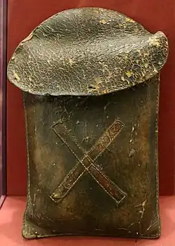 A brown leather case with a large oval flap and a diagonal cross, also in leather, stitched to the front