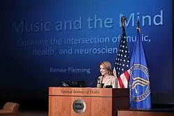 Fleming standing at a lectern, speaking