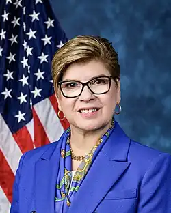 Official House portrait of Pou smiling in front of the U.S. flag, wearing a blue jacket with a floral inside, white shirt, and gold bead necklace.