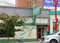 Photograph of a building's exterior with a doorway, mural of a tree, and a neon sign
