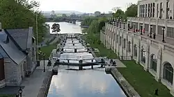 A small canal with a set of locks leading from a river near a large city.