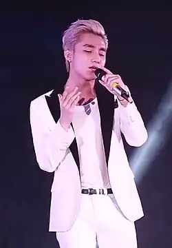 Tùng performing on stage, with blonde hair and a white suit