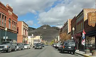 Color picture of a small American main street lined with small businesses, with a brownish hill visible at the end of the road