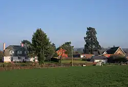 Several houses and school behind fields and hedgerows.