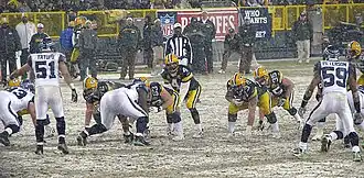 The Packers and Seahawks lined up on a snowy field as a play is about to start