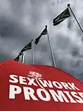 A red umbrella with the words 'sex work promise' on it, against a backdrop of South African flags