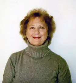 Polaroid of older woman smiling in light grey polar neck jumper.