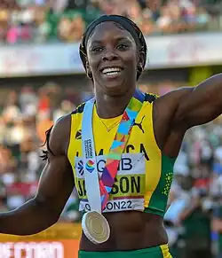 Jackson raising an arm with a gold medal draped around her neck