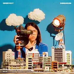 Ginger Root holding an old camera pointing at a model city