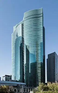 Ground-level view of a high-rise's curved, reflective glass facade; it is bisected by a vertical groove