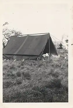 A black and white photograph of a tent in a grassy field.