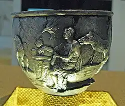 A male figure seated at a table, surrounded by a boar, eagle, and tortoise.