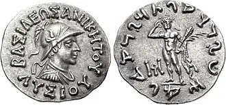 Another silver coin of Lysias. The obverse shows the king in uniform, wearing a crested Boeotian helmet and a royal diadem, with surrounding Greek legend. The reverse shows standing Heracles, and surrounding Kharosthi legend.