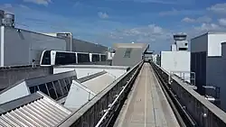 An empty concrete train guideway on the roof of an airport terminal building, with a train on the left traveling on a separate, parallel guideway.
